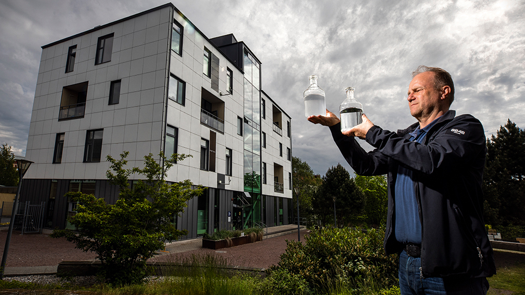 Per Ericson från Graytech visar skillnaden mellan gråvatten och det renade vattnet. I bakgrunden HSB Living Lab. Foto: Sören Håkanlind